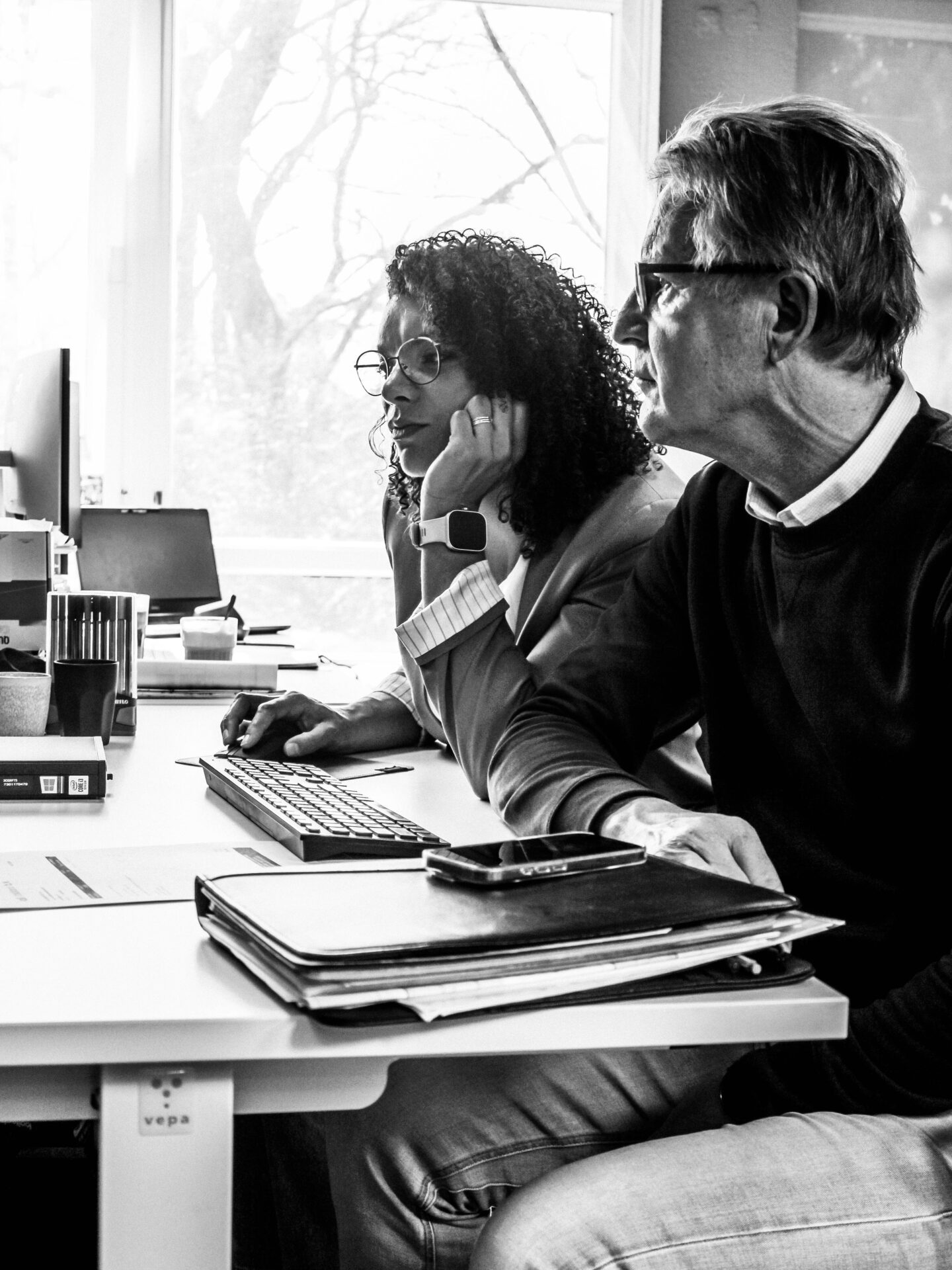 Zwart-witfoto van twee collega's die samen naar een beeldscherm kijken